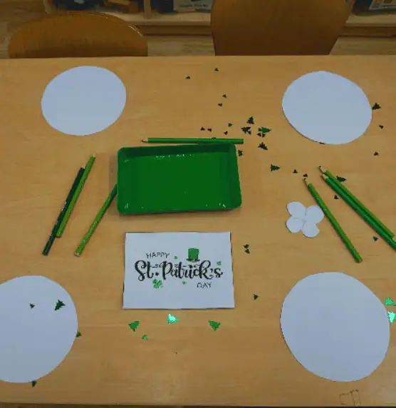 Green St. Patrick's Day craft table with paper shamrocks, green glitter, and drawing tools for children at Monkey Puzzle Day Nursery Enfield, celebrating St. Patrick's Day activities.