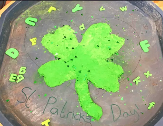 Green shamrock-shaped cake with green powder and alphabet sprinkles, celebrating St. Patrick's Day at Monkey Puzzle Day Nursery Enfield.