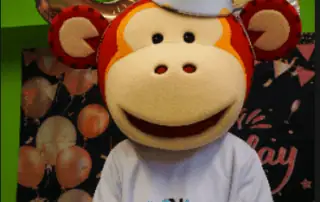 3_34825 Colorful monkey mascot with a birthday cake at Monkey Puzzle Day Nursery Enfield's celebration event.