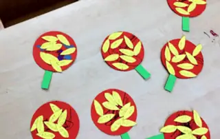 Red apple craft activity for preschool children at Monkey Puzzle Day Nursery Enfield, featuring paper apple shapes with child’s name tags and green leaf stems, engaging early learning and creativity.