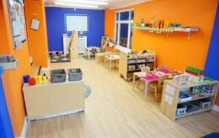 nursery facilities Colorful indoor playroom at Monkey Puzzle Day Nursery Enfield with vibrant orange and blue walls, children's tables, educational toys, and learning resources fostering early childhood development.