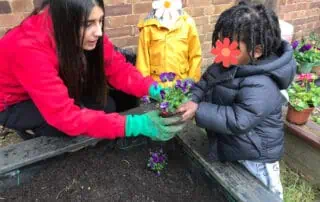 Colorful preschool children planting flowers in a garden at Monkey Puzzle Day Nursery Enfield.