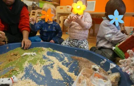 Colorful preschool children engaged in sensory play at Monkey Puzzle Day Nursery Enfield, exploring textured materials and small animal figurines, promoting early learning and development in a vibrant classroom setting.