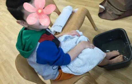 Child sitting in a wooden chair with feet soaking in a water basin at Monkey Puzzle Day Nursery Enfield, engaging in sensory play and water activity for early childhood development.