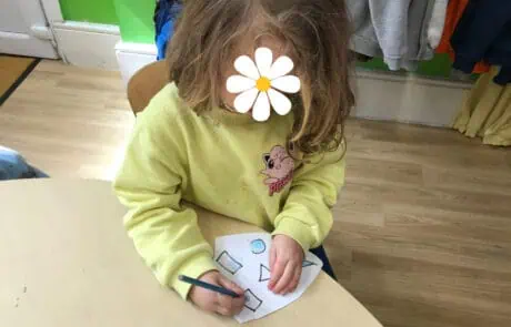 Colorful young girl drawing shapes on paper at Monkey Puzzle Day Nursery Enfield, engaging in early childhood education activities.