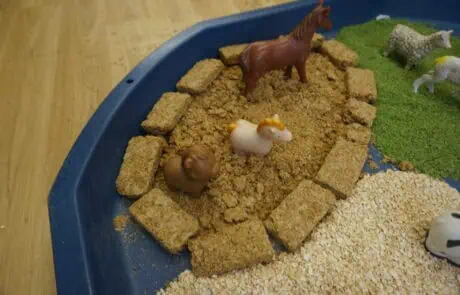 Kids imaginative play with toy farm animals in a nature-themed sand and gravel sensory tray at Monkey Puzzle Day Nursery Enfield.