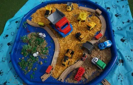 - Bright outdoor toy train set and construction vehicles on a blue sand and gravel play mat at Monkey Puzzle Day Nursery Enfield.