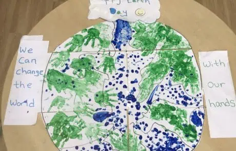 Hand-painted Earth Day collage with green handprints and blue paint dots, celebrating environmental awareness at Monkey Puzzle Day Nursery Enfield.