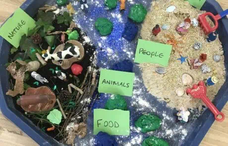 Colorful sensory bin representing nature, animals, and the ocean, with miniature figures and labeled signs celebrating Earth Day, designed for engaging preschool children at Monkey Puzzle Day Nursery Enfield.