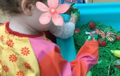 Colorful young child playing with butterfly and flower crafts at Monkey Puzzle Day Nursery in Enfield, engaging in creative outdoor activities for early childhood development.