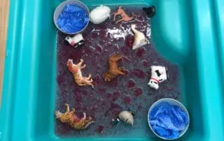 Colorful sensory water tray with toy animals and blue fabric, designed for children’s play and sensory exploration at Monkey Puzzle Day Nursery Enfield.