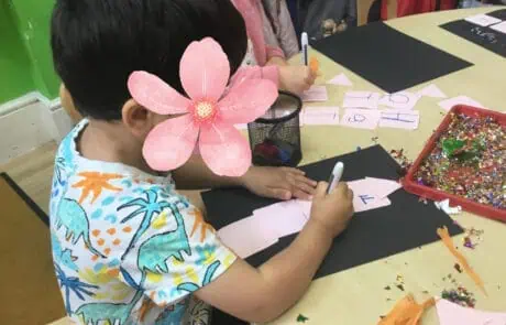Colorful preschool children engaging in arts and crafts activities at Monkey Puzzle Day Nursery Enfield, creating paper crafts with glitter and markers in a vibrant classroom setting.