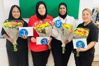 Brightly dressed nursery staff at Monkey Puzzle Day Nursery Enfield holding bouquets and numbered signs, celebrating a special occasion in a welcoming childcare environment.