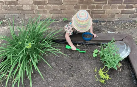 Child planting flowers in an outdoor garden at Monkey Puzzle Day Nursery Enfield, engaging in gardening activities for early childhood development and outdoor learning.