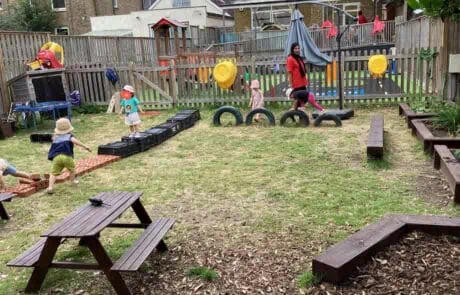 Colorful outdoor toddler playground at Monkey Puzzle Day Nursery Enfield with climbing structures and wooden benches.