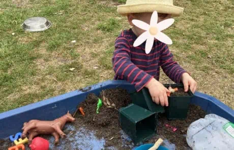 Bright young child playing in outdoor sensory and gardening activity at Monkey Puzzle Day Nursery Enfield, engaging in nature-based learning and imaginative play.