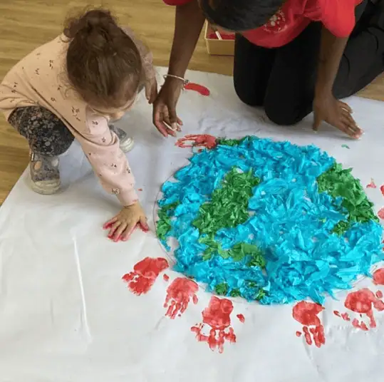 Colorful Earth art project with young children and teacher at Monkey Puzzle Day Nursery Enfield, fostering creativity and early learning.