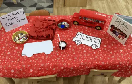 Colorful children's craft table decorated with themed items for Black History Month, including paper cutouts, buttons, and a toy bus, promoting diversity and cultural awareness at Monkey Puzzle Day Nursery Enfield.
