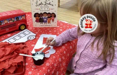 Little leaders book titled "Little Leaders: Bold Women in Black History" displayed on a table with a red vehicle toy and craft materials at Monkey Puzzle Day Nursery Enfield.
