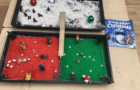 Miniature festive winter scene with snow, ornaments, and holiday decorations on a tray, visually appealing and engaging for children at Monkey Puzzle Day Nursery Enfield.