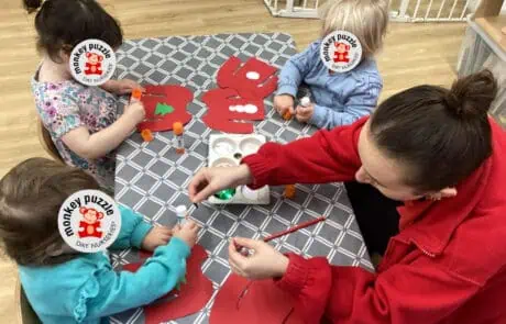 Colorful children engaging in a festive arts and crafts activity at Monkey Puzzle Day Nursery Enfield, creating holiday decorations with the guidance of a caring adult.