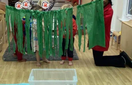 Colorful green streamers decorated around children and a teacher at Monkey Puzzle Day Nursery Enfield, engaging in a fun indoor activity.