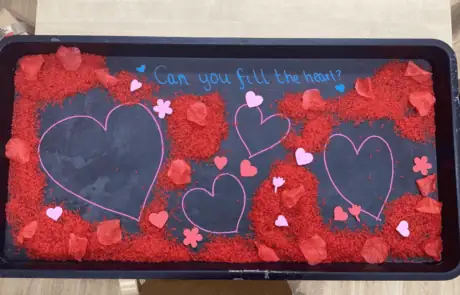 Hearts activity tray with red rice, paper flowers, and heart cutouts for children's creative learning at Monkey Puzzle Day Nursery Enfield.