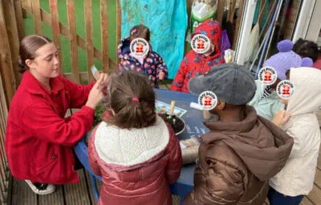 Colorful outdoor nursery play area at Monkey Puzzle Day Nursery Enfield, with children engaging in educational activities with an instructor during outdoor learning sessions.