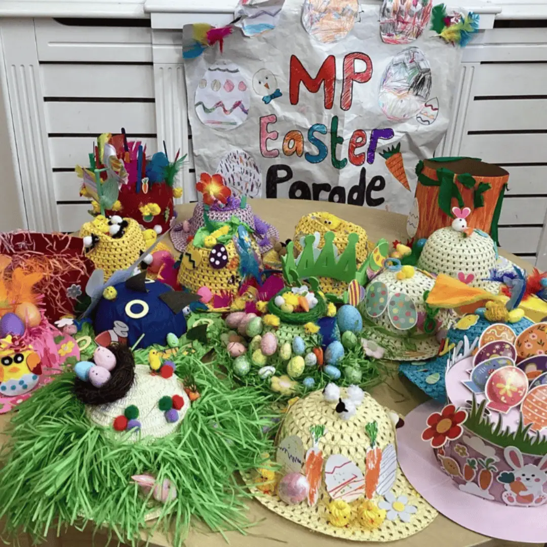 Colorful handmade Easter decorations and craft projects displayed on a table, with a "Monkey Puzzle Day Nursery Enfield" themed backdrop for an Easter parade celebration.