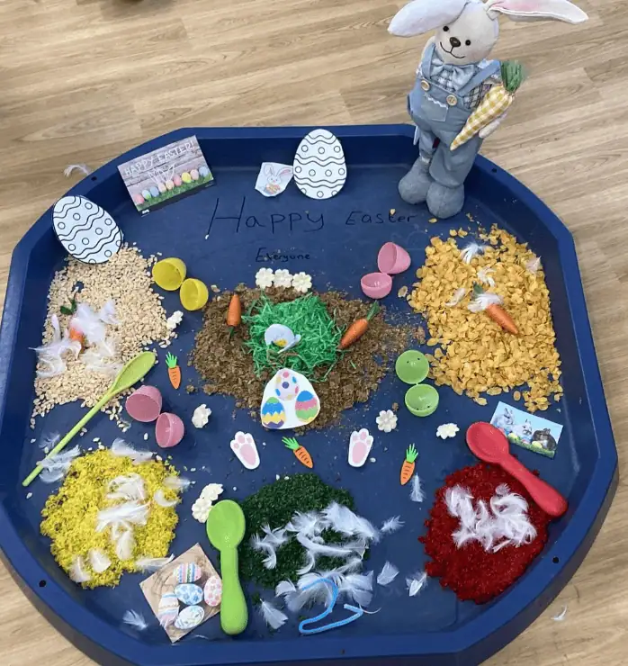 Colorful Easter-themed sensory tray with feathers, rice, pasta, and mini eggs, perfect for early childhood development at Monkey Puzzle Day Nursery Enfield.