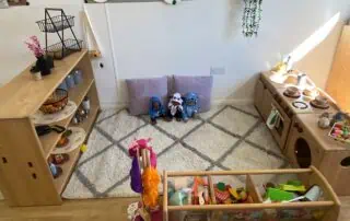 Monkey Puzzle Enfield Environment Colorful indoor play area with wooden kitchen set, shelves filled with toys, plush cushions, and playful decor, designed for children at Monkey Puzzle Day Nursery Enfield.