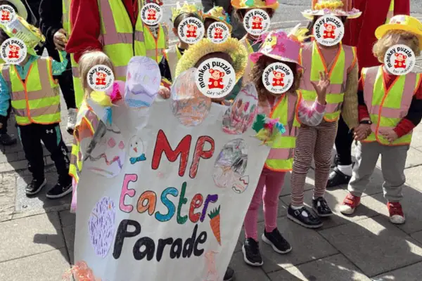 Easter parade at Monkey Puzzle Day Nursery Enfield featuring children in colorful costumes and a handmade sign.