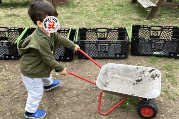 Child playing outdoors with a wheelbarrow at Monkey Puzzle Day Nursery Enfield, promoting outdoor activities and child development.
