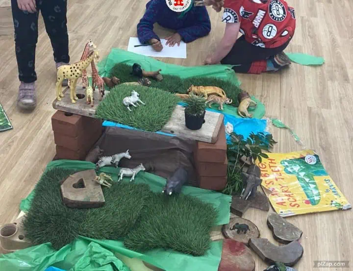 Giraffe and zebra toy figurines set up in a pretend jungle scene with children engaging in imaginative play at Monkey Puzzle Day Nursery Enfield.