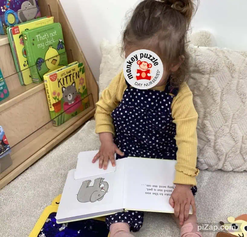 Monkey puzzle day nursery Enfield, showing a young girl reading a picture book with colorful children's books nearby, ideal for early childhood development and educational activities.