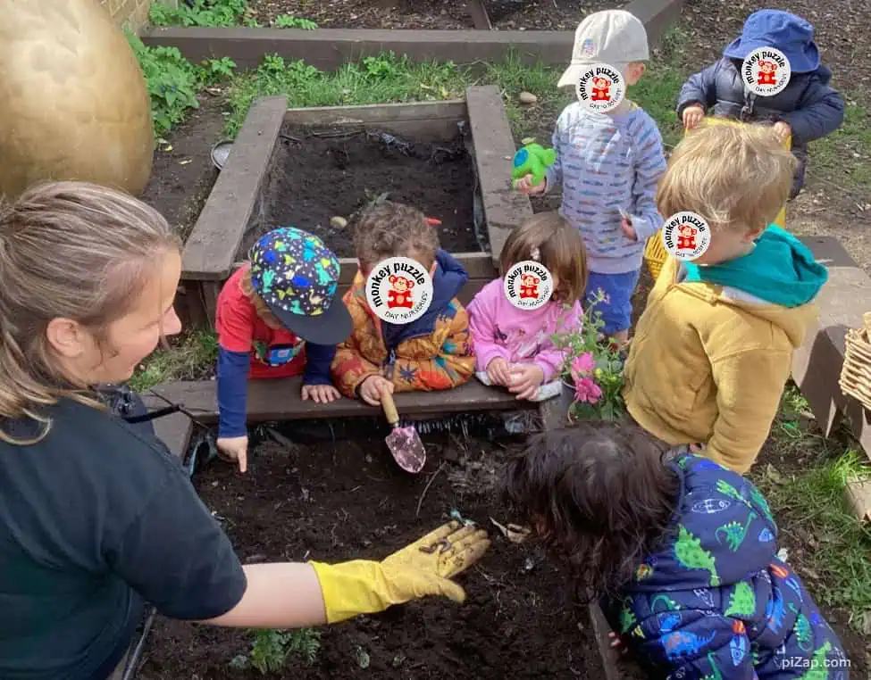 Children planting flowers in outdoor garden at Monkey Puzzle Day Nursery Enfield, engaging in nature-based activities for early childhood development.
