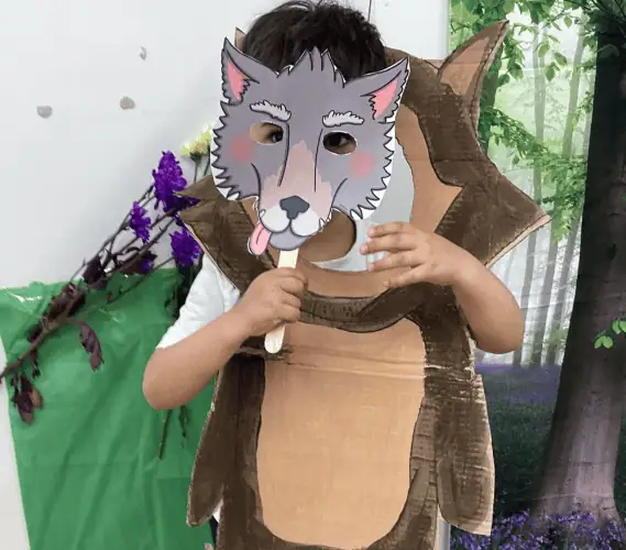 Smiling child in animal costume holding a wolf mask at Monkey Puzzle Day Nursery Enfield during a themed dress-up day.