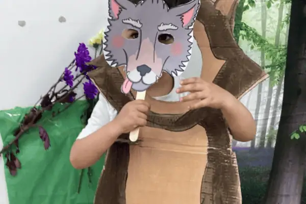 A child wearing a wolf mask and holding an ice cream stick, participating in a fun and imaginative activity at Monkey Puzzle Day Nursery Enfield.