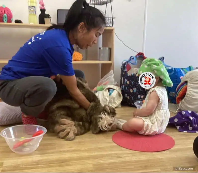 Friendly caregiver interacting with a young child and a friendly dog at Monkey Puzzle Day Nursery Enfield, fostering early socialization and development.