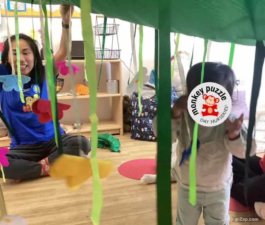 Monkey Puzzle Day Nursery Enfield children engaging in creative play under a colorful indoor play structure. Bright decorations and playful atmosphere promote early childhood development and fun learning experiences.