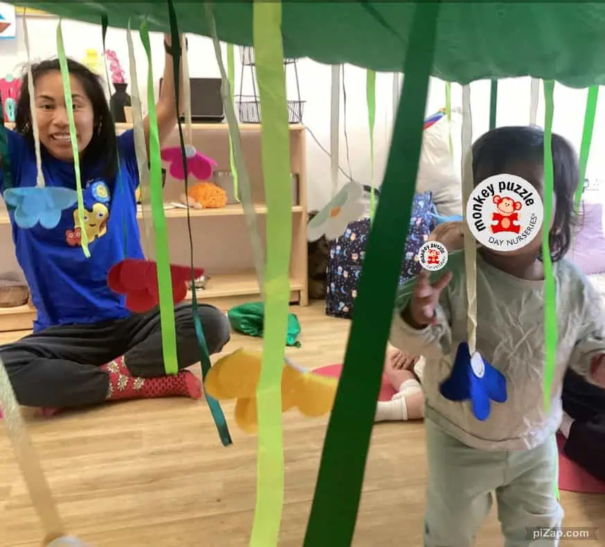 Wearable craft activity at Monkey Puzzle Day Nursery Enfield with children engaging in creative play under a colorful canopy.