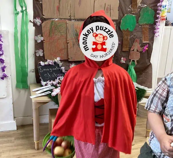 Monkey puzzle day nursery enfield kindergarten costume child dressed as Little Red Riding Hood with a book and classroom background.