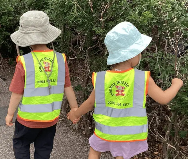 High-visibility children's vests with Monkey Puzzle Day Nursery Enfield logo, featuring kids exploring outdoors.