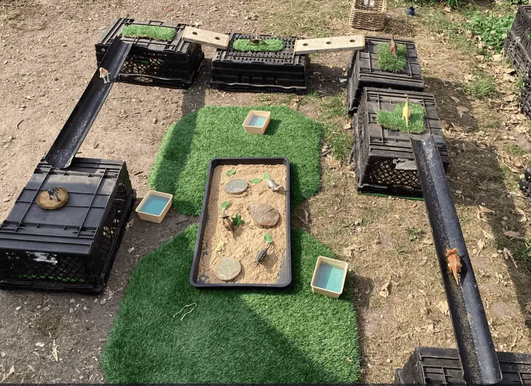 Sand and water play area with plastic crate tunnels and natural elements for children's outdoor exploration at Monkey Puzzle Day Nursery Enfield.