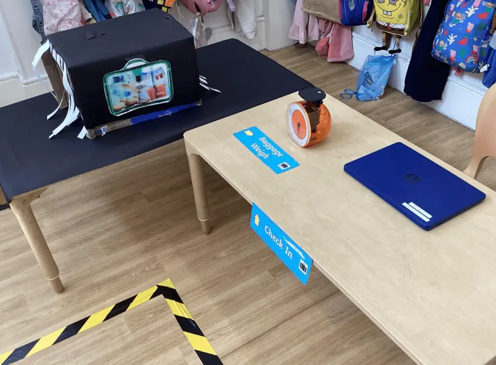 3_87369 Baggage check-in table at Monkey Puzzle Day Nursery Enfield, featuring a laptop, scale, and labeled signage for children and parents.