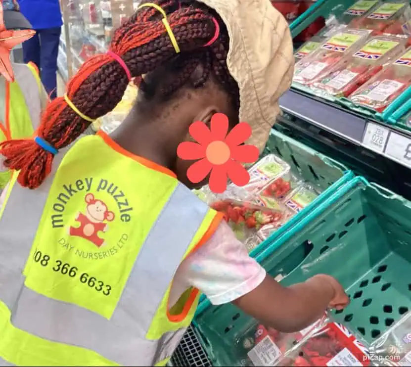 Fresh strawberries shopping at the supermarket, preschool girl wearing a high-visibility vest with Monkey Puzzle Day Nursery Enfield logo, promoting early childhood education and community engagement.