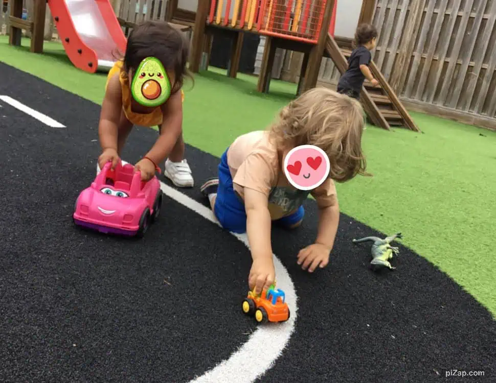Pink toy car with smiling face, kids playing outdoors at Monkey Puzzle Day Nursery Enfield, children engaging in active play on a black and green outdoor surface, fostering social skills and imagination at a trusted Enfield nursery.