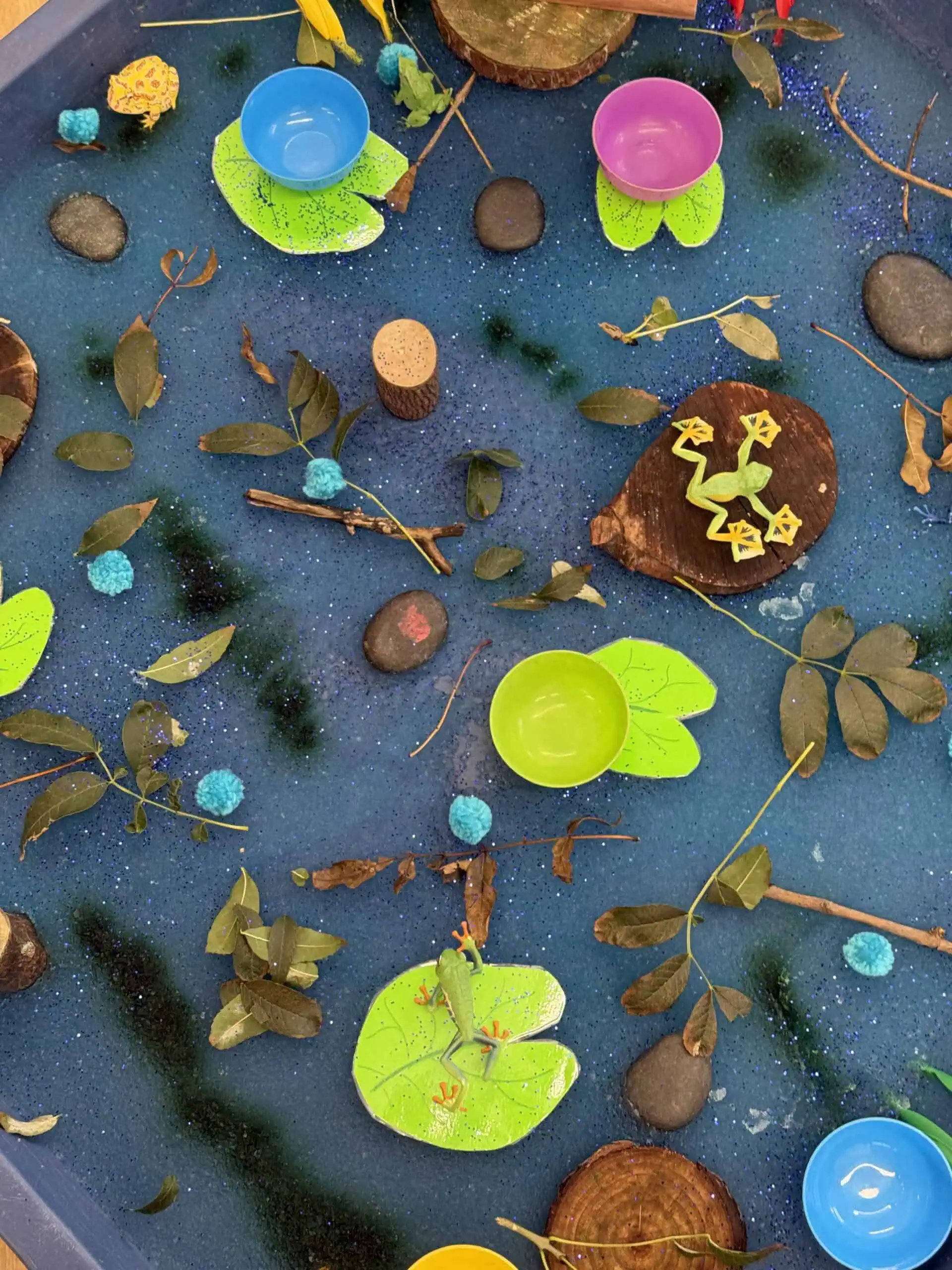 Colorful nature-inspired sensory play area with water, leaves, stones, and miniature cups, designed for early childhood development at Monkey Puzzle Day Nursery Enfield.