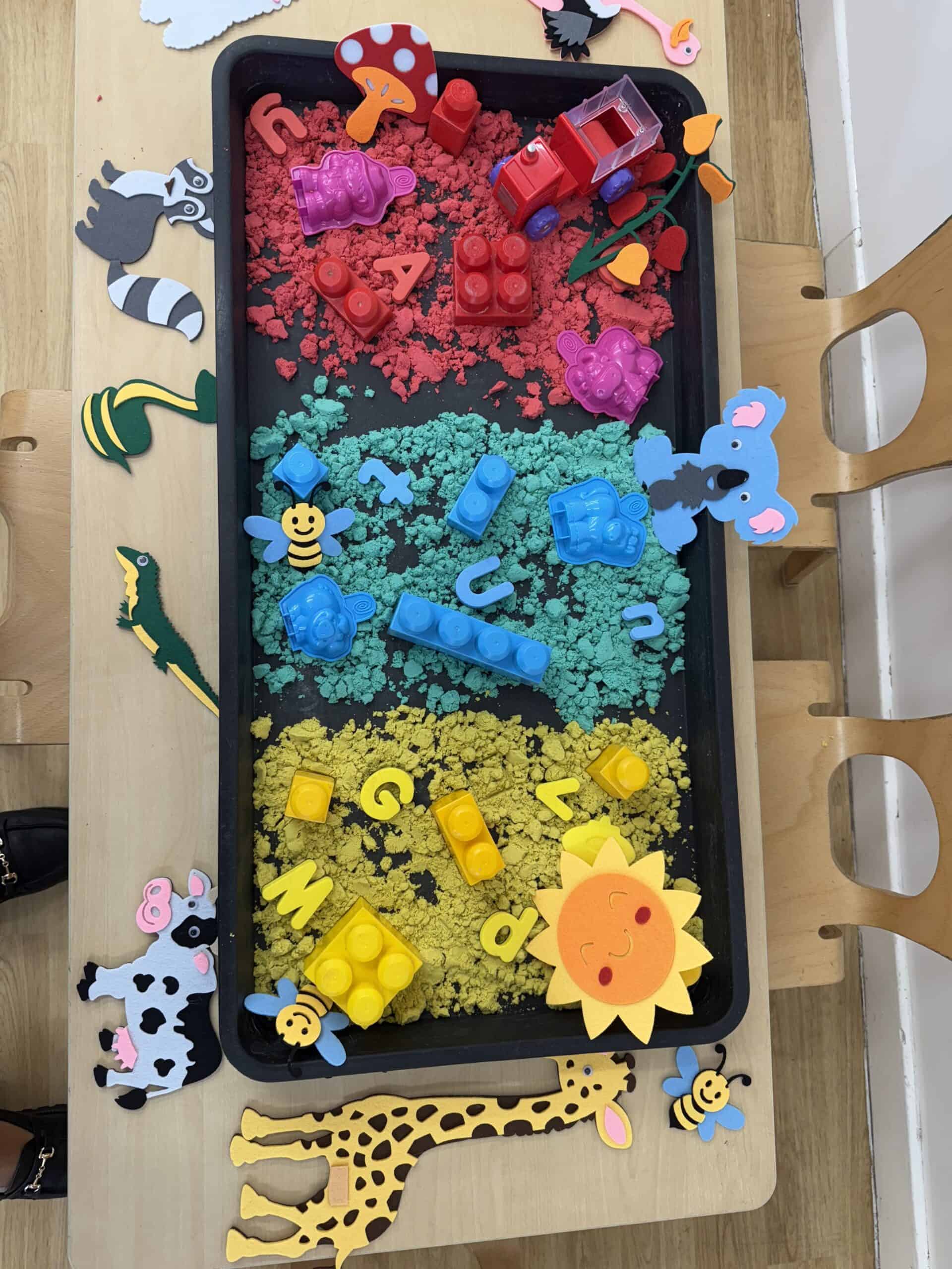 Colorful sensory play tray for children with animal-themed foam and LEGO blocks, featuring a rainbow design, to promote creativity and motor skills at Monkey Puzzle Day Nursery Enfield.