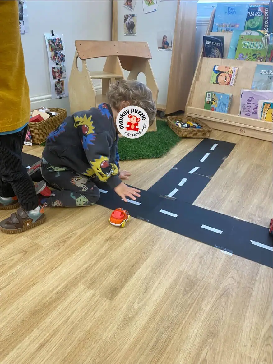 Colorful children playing with toy cars on a road-themed floor mat at Monkey Puzzle Day Nursery Enfield, engaging in imaginative and educational activities in a safe, nurturing environment.